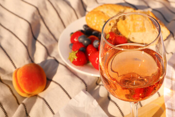 Glass of delicious rose wine and food on white picnic blanket, closeup