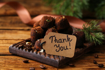 Chocolate sweets and tag with phrase Thank you on wooden table, closeup