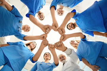 Doctor and interns holding fists together indoors, bottom view