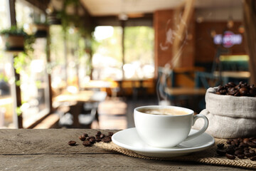 Cup of aromatic coffee and beans on wooden table in cafe, space for text