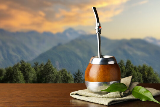 Calabash with mate tea and bombilla on wooden table outdoors at sunset. Space for text