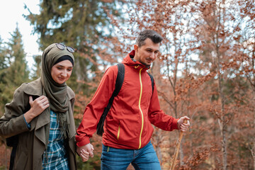 A young happy Muslim couple hiking in the autumn forest they are walking together with holding...
