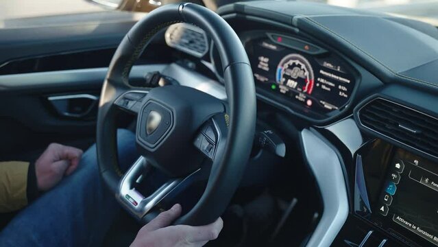 Driver steering wheel of sport car, man driving inside super sport car with illuminated dashboard and touchscreen functions. Person driving with high speed, road trip inside the sport car