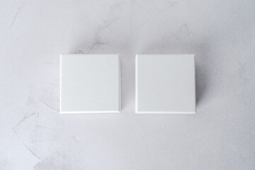 Two white square gift boxes mockup on gray concrete background. From above, top view, minimalist...