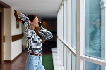 Young woman talking on the phone video call over the Internet online, smiling from a pleasant conversation near a window in the city
