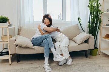 A man and a woman are sitting on the couch at home wearing white T-shirts and hugging each other with smiles. Family life lifestyles of young marrieds