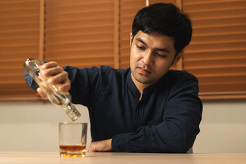 Alcoholism, depressed asian young man pouring, holding bottle whiskey into the glass, drinking alcohol  beverage at night. Treatment of alcoholic addiction, suffer abuse problem alcoholism concept.