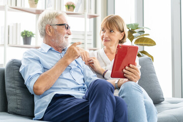 Happy husband and wife senior couple elderly family, caucasians mature, adult lover and retired man, woman using tablet communicating, shopping online, reading news on sofa at home together.