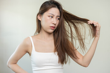 Damaged Hair, frustrated asian young woman, girl hand in holding splitting ends, messy unbrushed dry hair with face shock, long disheveled hair, health care of beauty. Portrait isolated on background.