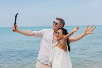 Beautifull wedding couple kissing and embracing on the beach. Multiracial young loving couple taking a selfie together on smartphone on beach