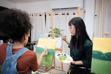Female Asian teacher teaches and demonstrates to a student girl on acrylic color picture painting...