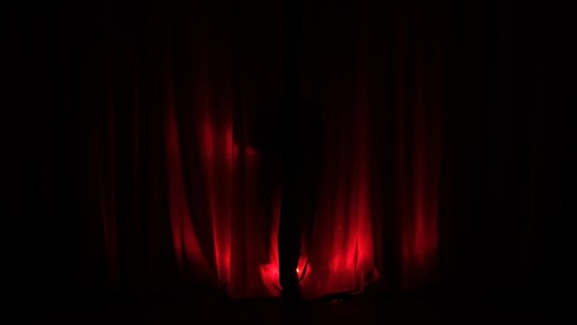 Elegant dancer, actress woman in enters the stage in a dark red background with circle light focusing on her