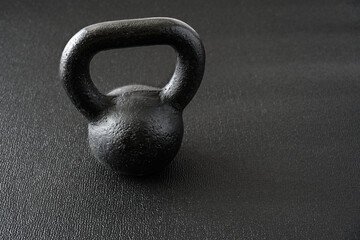 Naklejka na ściany i meble Simple fitness, black iron kettlebell on a black gym floor 