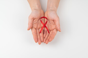 Female hands with a red ribbon on a white background. Symbol of the fight against AIDS. 