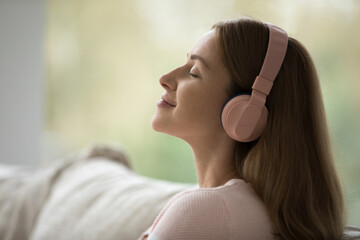 Side view face serene woman wear headphones enjoy music, feel carefree looks peaceful, close up....