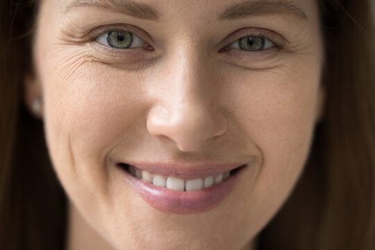 Cropped close up part of female face front view, young 30s woman portrait look at camera, having white-toothed smile, wrinkles around eyes, staring at you. Natural beauty, advertise skincare treatment