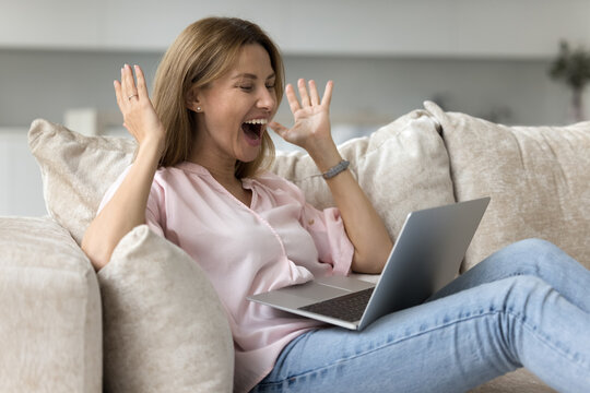 Young happy woman staring at laptop screen feels overjoyed get great profitable commercial offer, winning on-line lottery, feels incredible happy, relish victory seated on sofa at home, celebrate luck