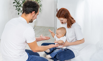Obraz premium dad and mom play with their son. a child in a white t-shirt and blue jeans crawls on the floor. family in studio or at home