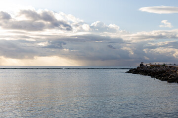 vue sur un quai en pierre en bord d'océan lors d'un lever de soleil avec de la pluie au loin