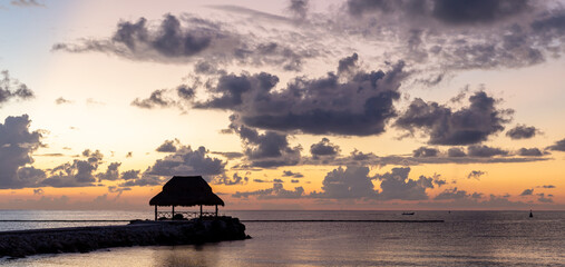Naklejka na ściany i meble silhouette d'une cabane avec un toit de paille sur la mer lors d'un lever de soleil très coloré
