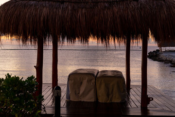 petite cabane avec un toit de paille avec vue sur la mer lors d'un lever de soleil avec des tables...