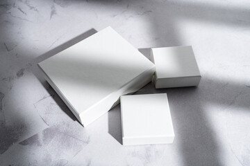 Three white square gift boxes mockup on gray concrete background. From above, shadow overlay, closeup,  top view, minimalist concept