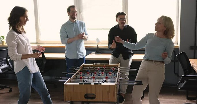 Group of diverse businesspeople having great time together during break. Happy carefree office employees, older and younger workmates play table soccer or foosball in workplace, enjoy victory and rest