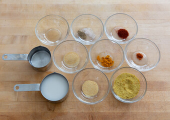 Looking down at a cup of coconut milk and various spices, such as tumeric, nutritional yeast, paprika, garlic, salt, pepper on wooden cutting board.  