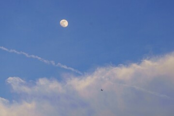 Scenic view of the Full Moon in the blue sky covered in white puffy clouds in daylight