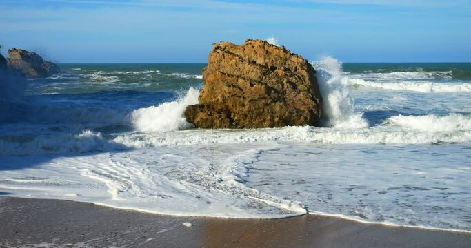Swell breaking on the beach of Biarritz in the Basque Country with the lighthouse on the horizon (in slow motion)