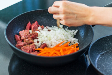 Close up shot of a beef, carrots and chopped onion in the pot. Meal