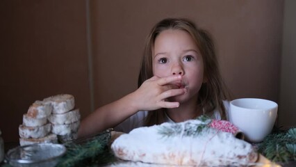 a little girl tries powdered sugar with her finger from a Christmas stollen while sitting at the table.