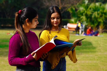 Fototapeta na wymiar Two Indian female students talking each other while reading books