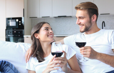 Young loving couple drinking a glass of red wine in their living room.