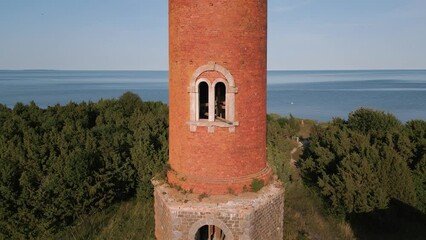 Ascending flight up along a old lost place lighthouse without windows and old roof at the coast of baltic sea - Estonia in Europe - nature helicopter flyover establishing shot summer 2022 - bird view