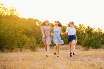 Fototapeta premium A group of girlfriends jumps and runs outdoors. A group of female friends hugs and enjoys the sunset in nature. Laughter, smiles and joy.