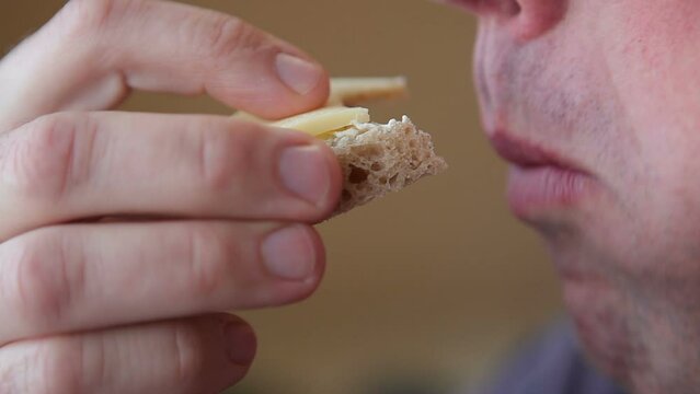 A hungry man greedily eats a cheese sandwich. The man is having breakfast.