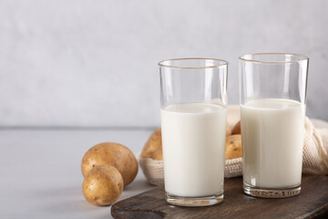 Vegan plant based milk in two transparent glasses. Alternative potato milk and potato tubers on gray table