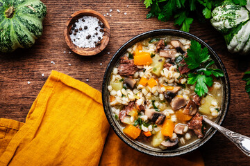 Autumn food. Warming soup with pumpkin, mushrooms, vegetables, beef and barley. Rustic wood table background, top view