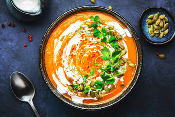 Spicy vegan pumpkin soup with pumpkin seeds, coconut cream and pea sprouts. Winter or autumn healthy vegetarian food. Soup bowl on blue table background. Top view