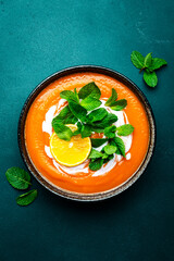 Sweet vegan pumpkin soup with coconut cream, orange and mint. Winter or autumn healthy vegetarian comfort food. Soup bowl on green table background. Top view