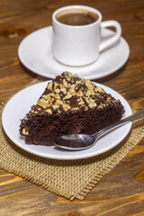 Piece of chocolate cake brownie and a spoon. A Cup of hot coffee with steam in the background. Calories in a piece of chocolate cake