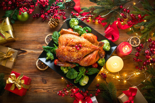Christmas Dinner. Roasted chicken. Winter Holiday table served, decorated with candles and xmas baubles. Roast turkey over wooden background with Christmas tree, table setting family dinner with gifts