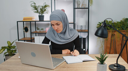 Muslim business woman in hijab study with notebook at home office on laptop computer making conference video call talking to webcam. Online teacher e-learning in remote chat. Distance education online