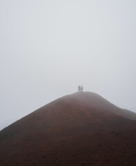 Low angle shot of a two people on a mountain top covered with fog during the winter season