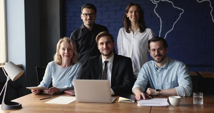 Group of businesspeople sit stand in workspace with modern devices smile look at camera, pose for corporate photo. Portrait of five successful professionals employees. Career, business and leadership