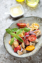 Bowl with panzanella or italian tomato and bread salad, vertical shot on light-brown granite background, middle close-up