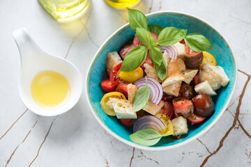 Turquoise bowl with italian panzanella salad on a light-beige stone background, elevated view, horizontal shot