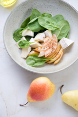Salad with fresh spinach leaves, pear and camembert slices, vertical shot on a light-beige marble background, elevated view, middle close-up