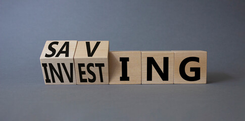 Saving and Investing symbol. Turned wooden cubes with words Investing and Saving. Beautiful grey...
